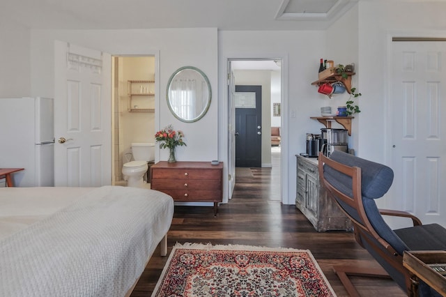 bedroom featuring freestanding refrigerator, dark wood-style flooring, and ensuite bath