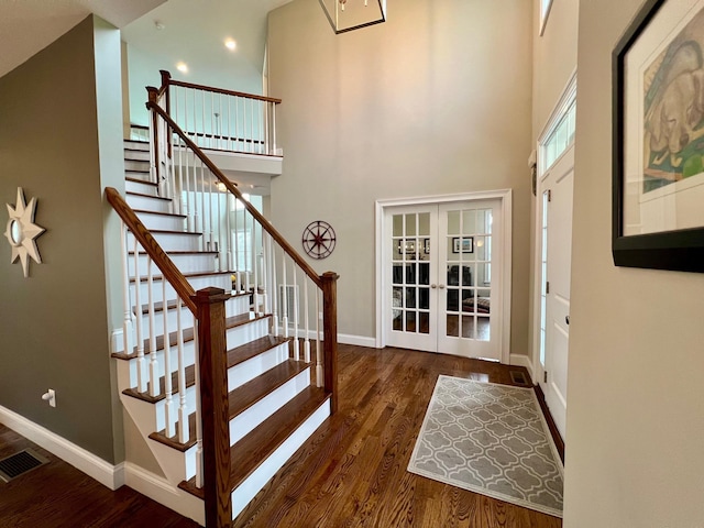 foyer entrance with a towering ceiling, baseboards, visible vents, and wood finished floors