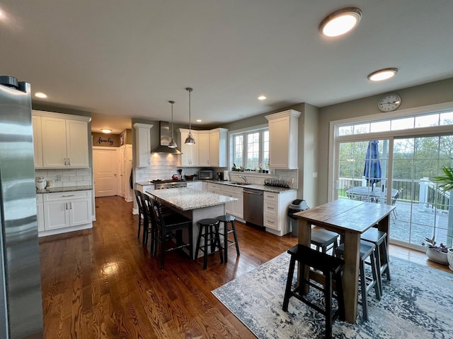 kitchen featuring wall chimney exhaust hood, appliances with stainless steel finishes, a kitchen breakfast bar, and dark wood finished floors