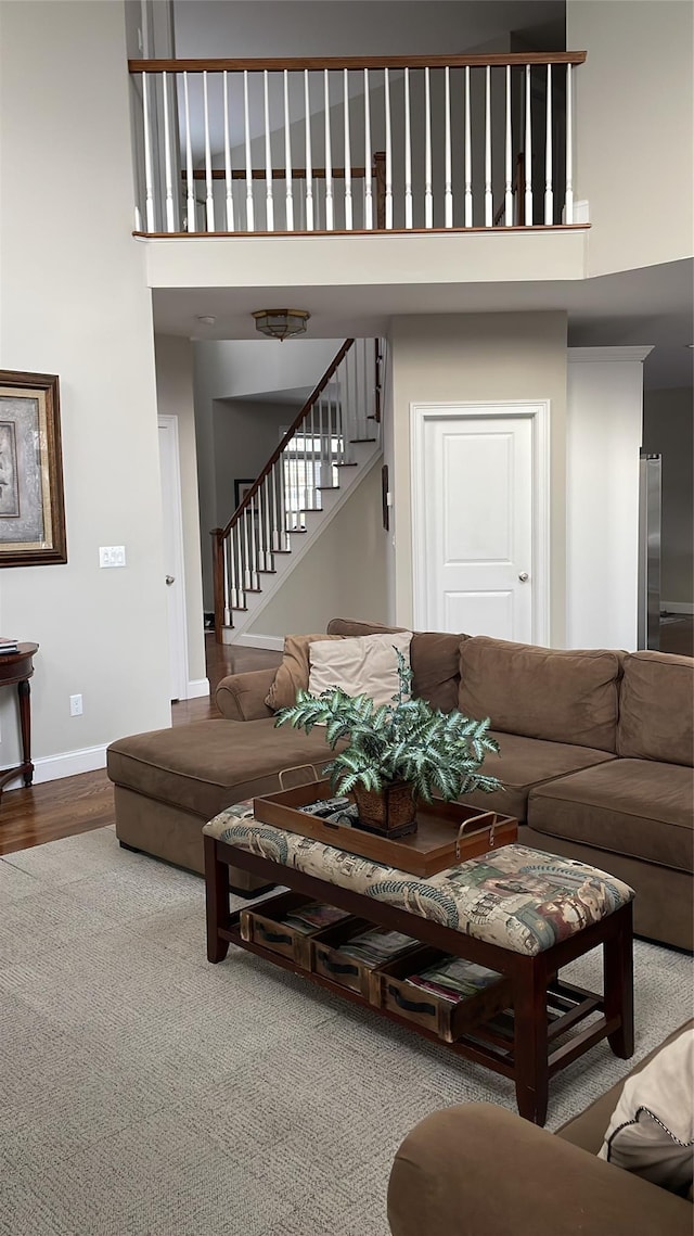 living area featuring wood finished floors, baseboards, a high ceiling, and stairs