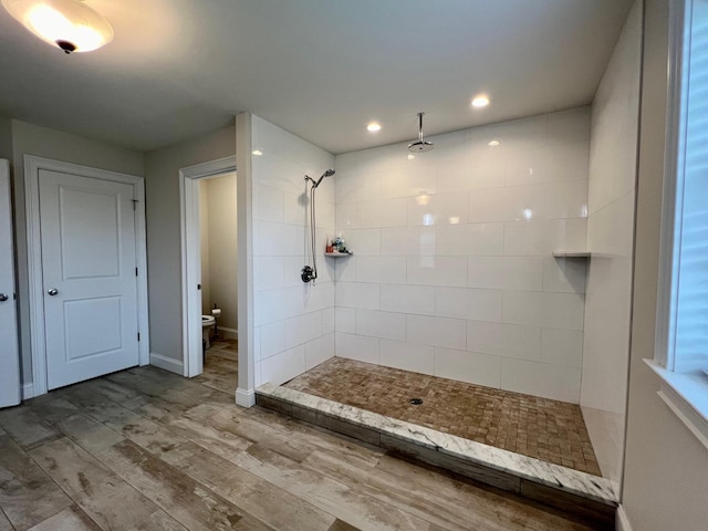 bathroom featuring baseboards, toilet, wood finished floors, a tile shower, and recessed lighting