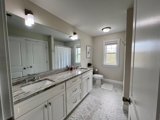 bathroom featuring toilet, a sink, baseboards, and double vanity