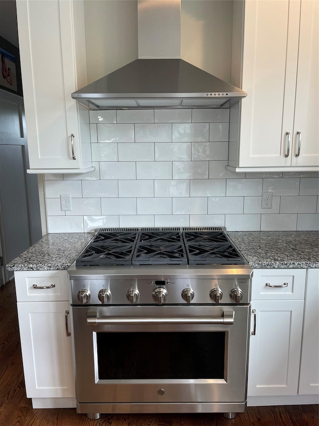 kitchen with high end stove, stone counters, wall chimney exhaust hood, and white cabinets