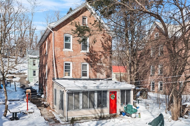 snow covered property featuring brick siding and a sunroom