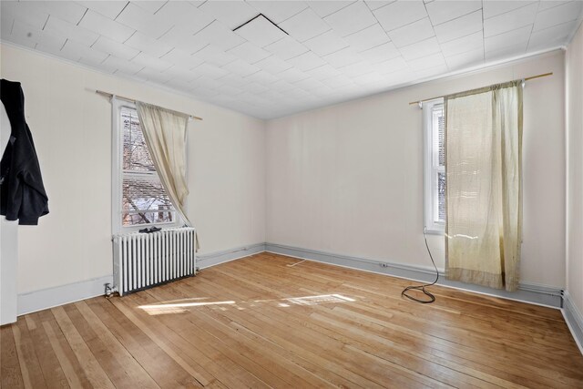 unfurnished room with baseboards, hardwood / wood-style floors, and radiator heating unit