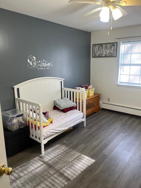 bedroom with ceiling fan, baseboard heating, and wood finished floors