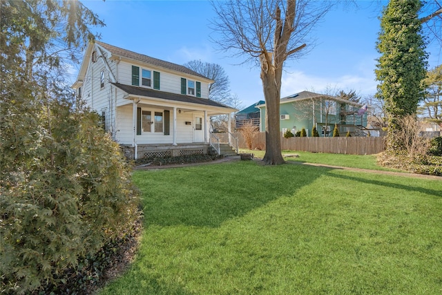 view of front facade with covered porch, a front lawn, and fence