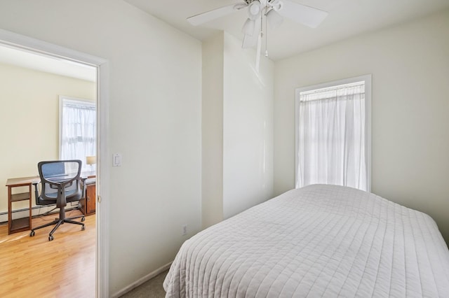 bedroom featuring light wood finished floors, baseboards, and a baseboard heating unit