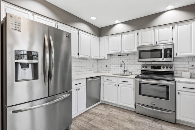 kitchen with light wood-style flooring, appliances with stainless steel finishes, a sink, white cabinetry, and backsplash