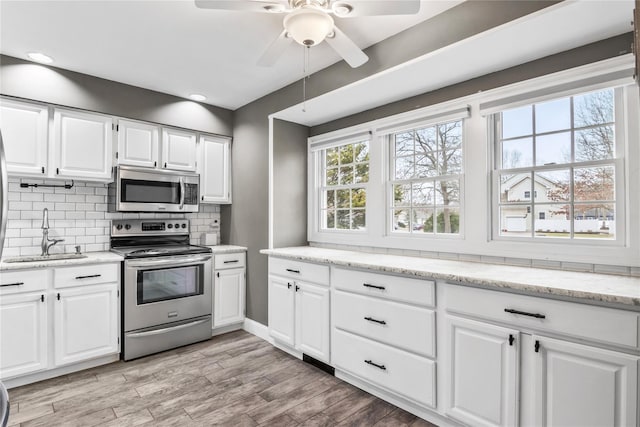 kitchen featuring light wood-style flooring, stainless steel appliances, a sink, white cabinets, and backsplash