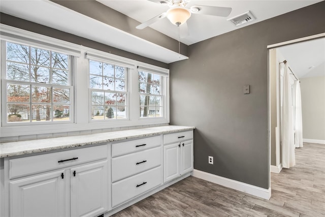 bar featuring light wood finished floors, baseboards, visible vents, and a ceiling fan