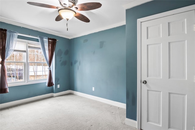 carpeted spare room with ornamental molding, baseboards, and a ceiling fan