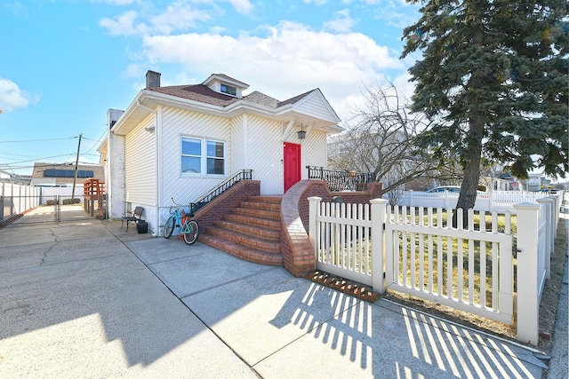 view of front of property with a shingled roof, a fenced front yard, a chimney, and a gate