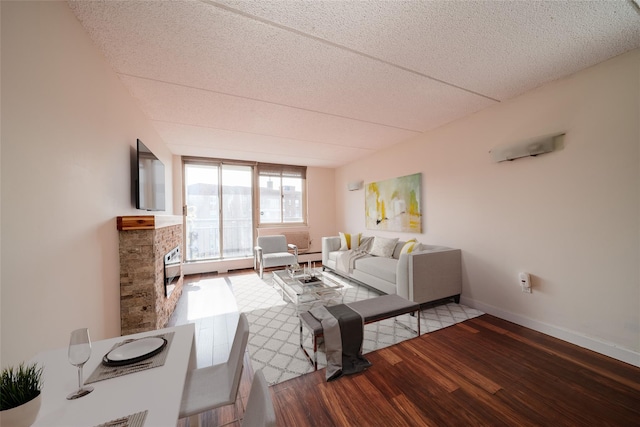 living room with a baseboard heating unit, a fireplace, baseboards, and wood finished floors