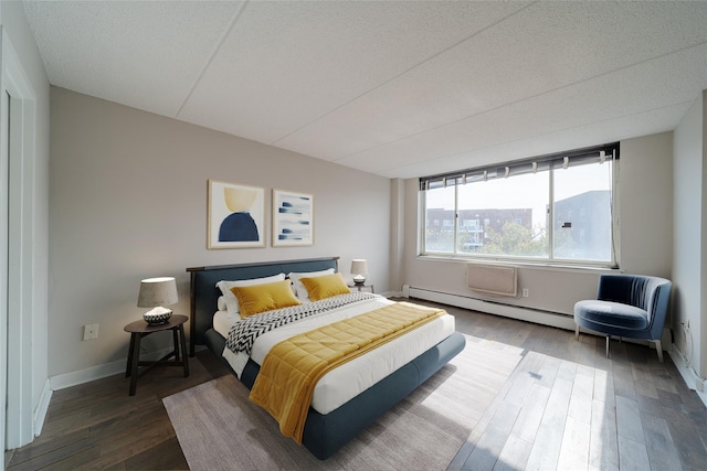 bedroom featuring a baseboard heating unit, wood finished floors, and baseboards