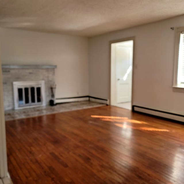 unfurnished living room with a baseboard heating unit, baseboard heating, wood finished floors, and a glass covered fireplace