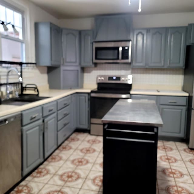 kitchen with stainless steel appliances, gray cabinets, a kitchen island, and a sink