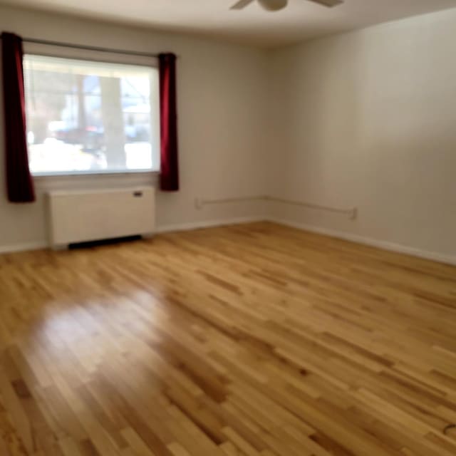 spare room with ceiling fan, light wood finished floors, radiator heating unit, and baseboards