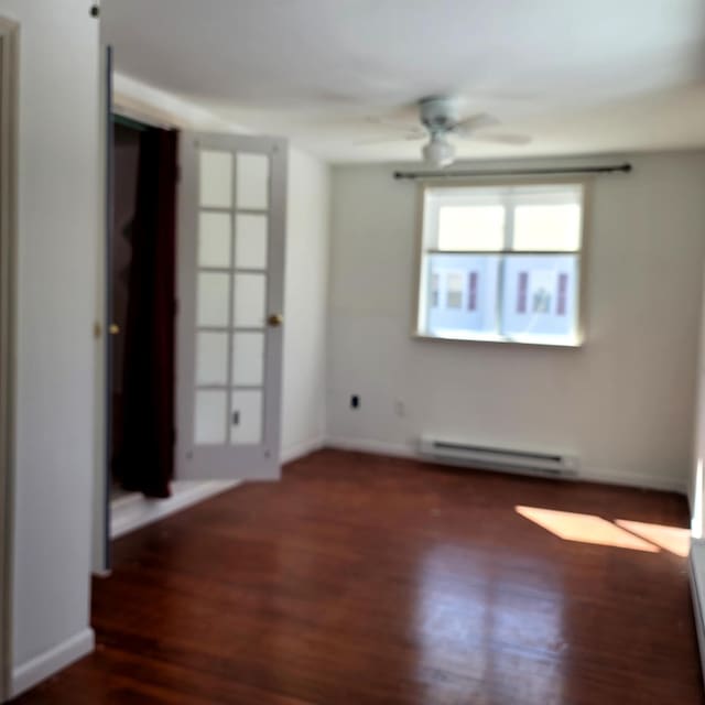 spare room featuring ceiling fan, baseboard heating, wood finished floors, and baseboards