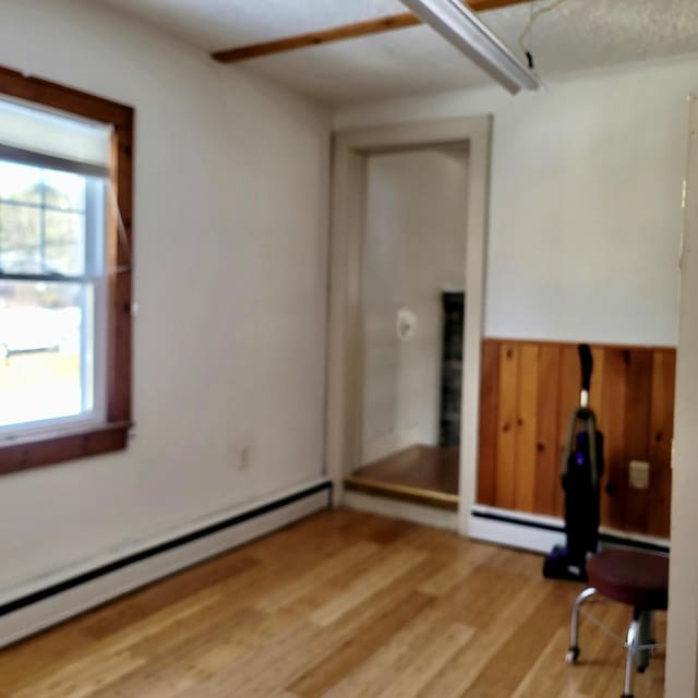 spare room featuring a wealth of natural light, a baseboard radiator, a wainscoted wall, and light wood finished floors