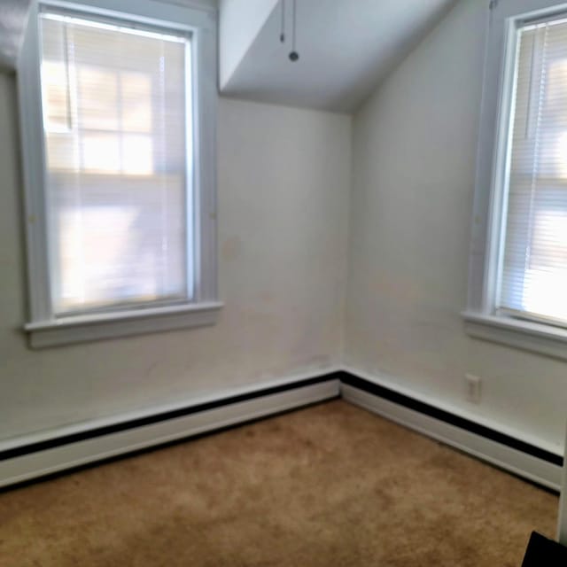 interior space featuring lofted ceiling, a baseboard heating unit, carpet floors, and plenty of natural light