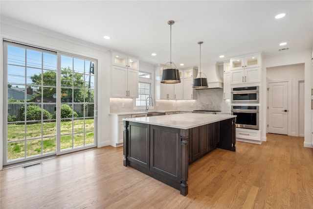 kitchen featuring double oven, custom range hood, light wood finished floors, and white cabinetry