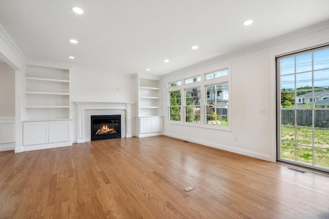 unfurnished living room featuring built in shelves, visible vents, a wealth of natural light, and a glass covered fireplace