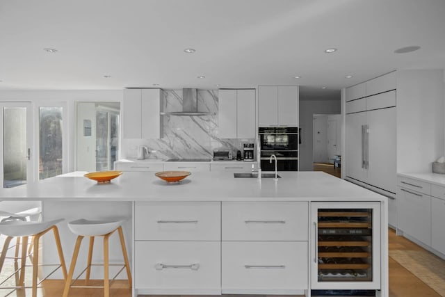 kitchen with beverage cooler, a kitchen island with sink, white cabinetry, and light countertops