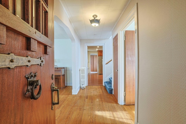 hall with wallpapered walls, baseboards, light wood-style flooring, radiator heating unit, and stairs