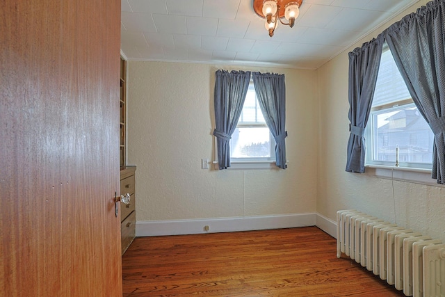 empty room with radiator, baseboards, wood finished floors, and a textured wall