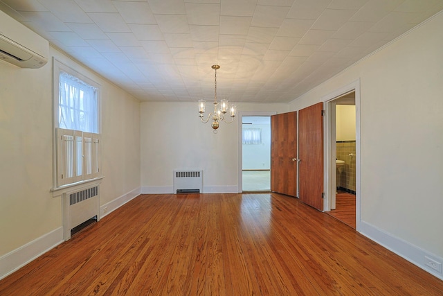 empty room with radiator heating unit, baseboards, wood finished floors, and a wall mounted air conditioner