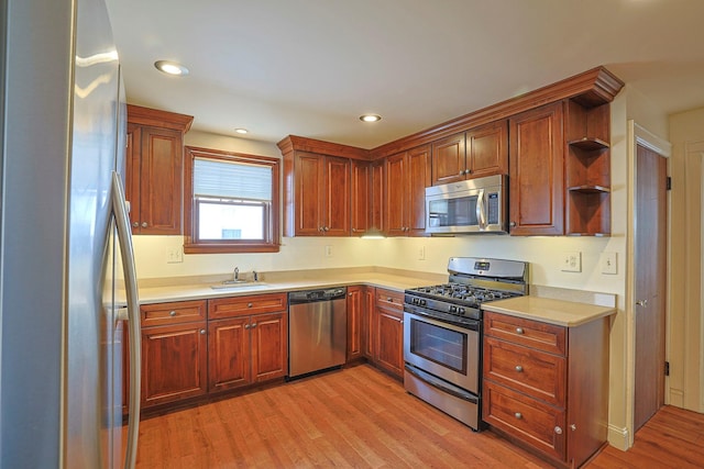 kitchen with open shelves, stainless steel appliances, light countertops, a sink, and light wood-type flooring