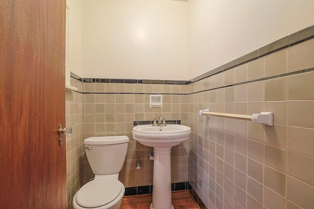 half bath with toilet, a wainscoted wall, a sink, and tile walls