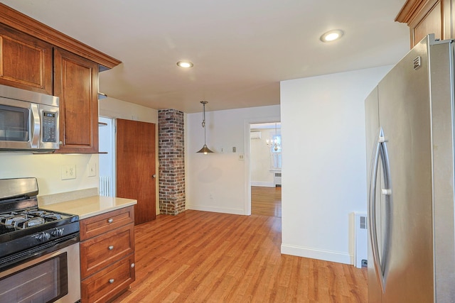 kitchen with light wood finished floors, brown cabinetry, appliances with stainless steel finishes, decorative light fixtures, and light countertops