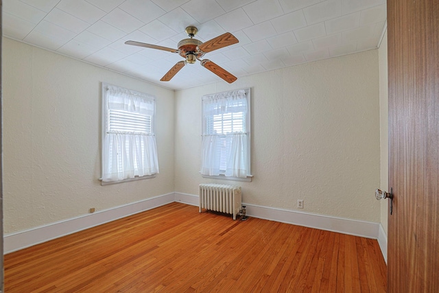 unfurnished room featuring baseboards, a ceiling fan, a textured wall, radiator, and wood finished floors