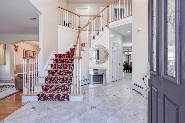 foyer entrance featuring a towering ceiling, a baseboard radiator, stairway, and baseboards