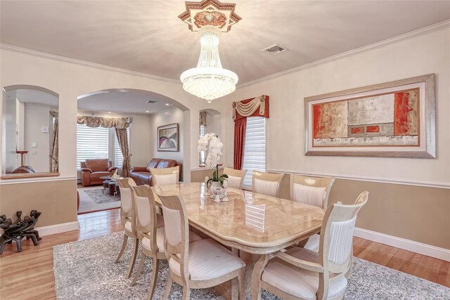 dining room featuring ornamental molding, light wood-type flooring, visible vents, and a notable chandelier