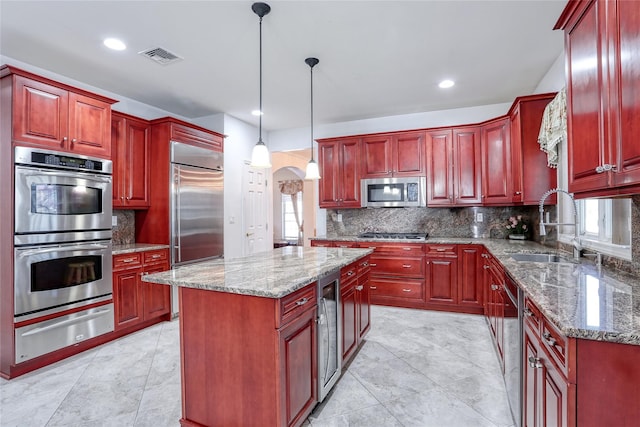 kitchen featuring arched walkways, stainless steel appliances, dark brown cabinets, a sink, and a warming drawer