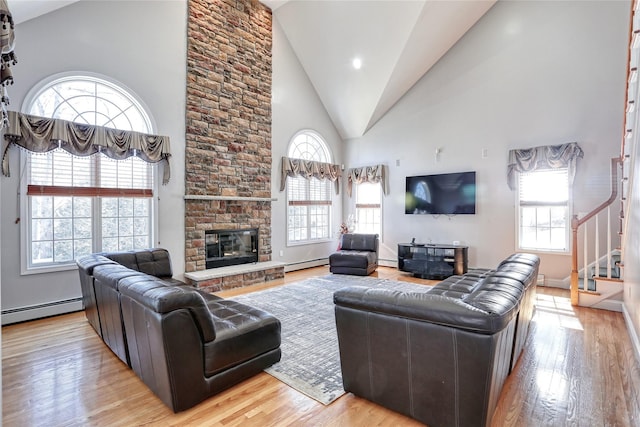 living area with stairway, a baseboard heating unit, wood finished floors, and a stone fireplace