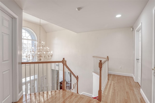 hall with a notable chandelier, vaulted ceiling, an upstairs landing, wood finished floors, and baseboards