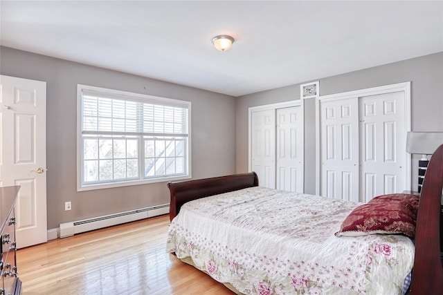 bedroom with a baseboard heating unit, wood finished floors, and two closets