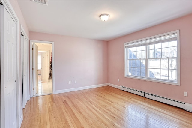 unfurnished bedroom with visible vents, baseboard heating, light wood-style flooring, and baseboards