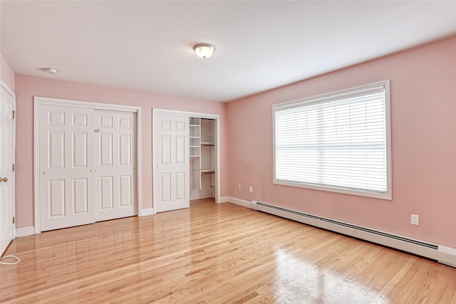 unfurnished bedroom with multiple closets, a baseboard radiator, light wood-type flooring, and baseboards