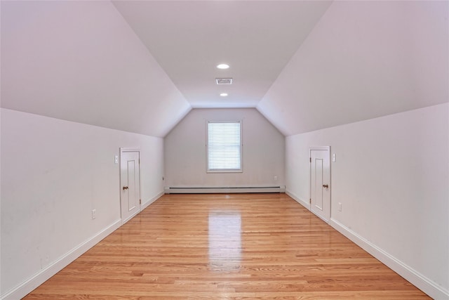 additional living space featuring visible vents, baseboards, lofted ceiling, a baseboard radiator, and light wood-style flooring