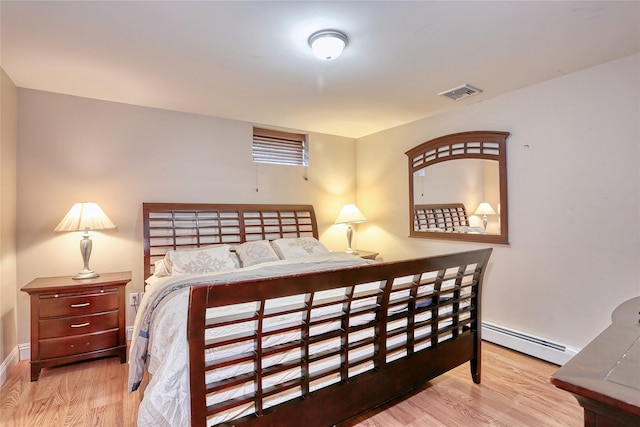 bedroom with baseboard heating, wood finished floors, visible vents, and baseboards