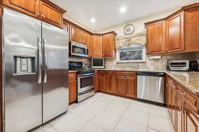 kitchen with brown cabinetry, appliances with stainless steel finishes, a toaster, and light stone counters