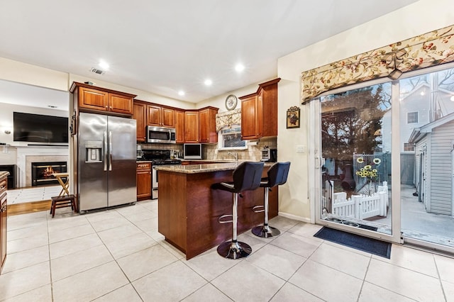 kitchen with a peninsula, stone counters, a kitchen bar, decorative backsplash, and appliances with stainless steel finishes