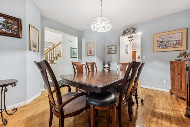 dining area with light wood-type flooring, baseboards, a notable chandelier, and stairway