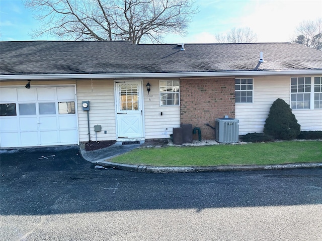 entrance to property with central air condition unit, a yard, a garage, and roof with shingles