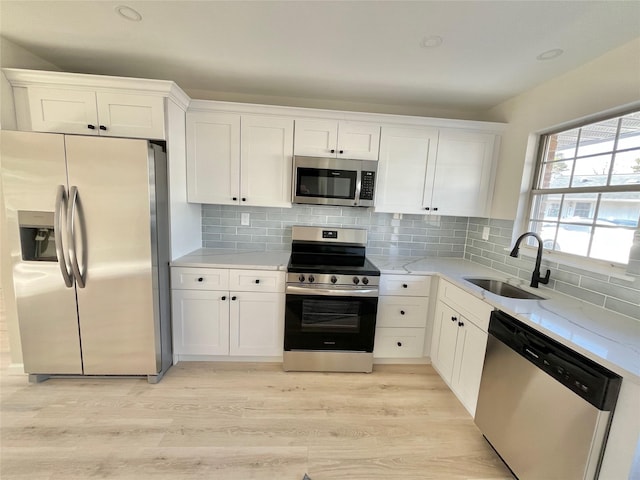 kitchen featuring white cabinets, light wood-type flooring, stainless steel appliances, and a sink